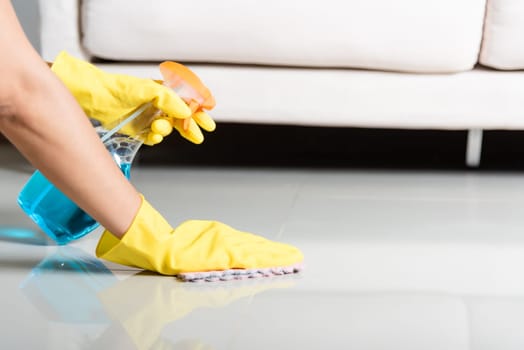 Asian woman wearing yellow rubber glover with cloth rag and detergent spray cleaning floor at home in living room, Female hands wash cleaner, housework and housekeeping concept