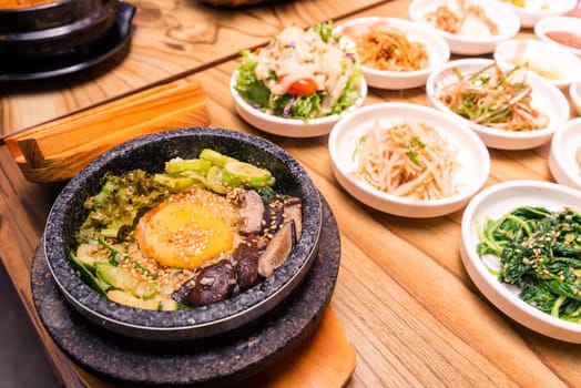 Bibimbap in a black heated stone bowl, Korean traditional dish- bibimbap mixed rice with vegetables Include beef and fried egg and pickles set on table, Japanese hot pot food