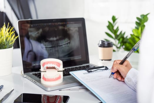 Oral dental. Dentist doctor in uniform writing information of patient in paperwork checklist on clipboard on desk office, teeth model, X-ray on laptop screen, prescription medical dental healthcare