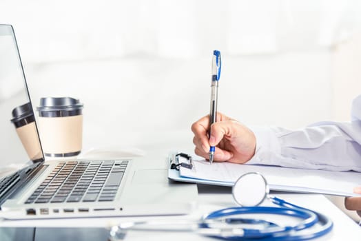 Doctor or nurse in uniform with stethoscope writing something information of patient prescription medical in paperwork checklist on clipboard on front laptop computer, medication history record