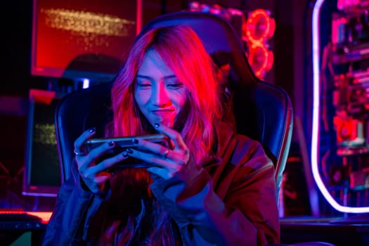 Asian woman live stream she play video game via smartphone at home neon lights living room, Gamer playing online game application on mobile phone wear gaming headphones, E-Sport concept