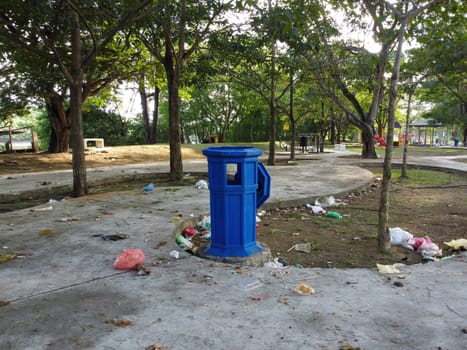 Blue dustbin and some garbage on floor at the park