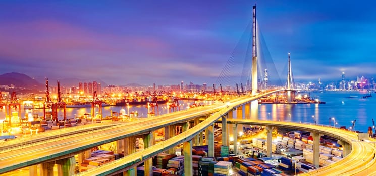 Container Cargo freight ship with working crane bridge in shipyard under Stonecutters highway bridge at sunset for Logistic Import Export, Hong kong