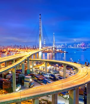 Container Cargo freight ship with working crane bridge in shipyard under Stonecutters highway bridge at sunset for Logistic Import Export, Hong kong