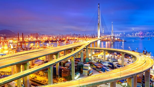 Container Cargo freight ship with working crane bridge in shipyard under Stonecutters highway bridge at sunset for Logistic Import Export, Hong kong
