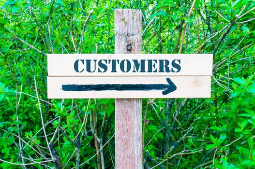 CUSTOMERS written on Directional wooden sign with arrow pointing to the right against green leaves background. Concept image with available copy space