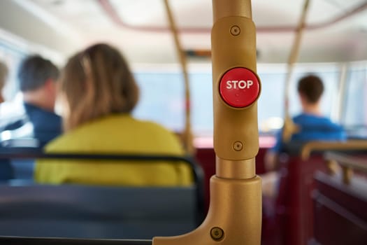 Detail of red stop button inside double decker bus in London, UK, with passengers seated in the blurred background.