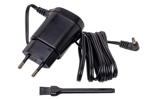 Closeup of a black AC to DC power adapter or charger for a rechargeable beard and hair clipper and a cleaning brush isolated on white background. Macro.