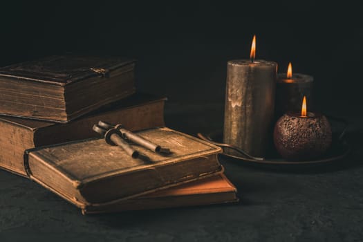 Pile of old antique books with candle and old rusty keys in vintage style on black background