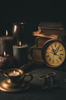 Candles, antique books, old clock and old rusty keys in vintage style on black background