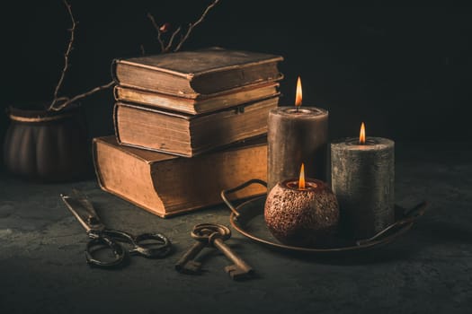 Pile of old antique books with candle and old rusty keys in vintage style on black background