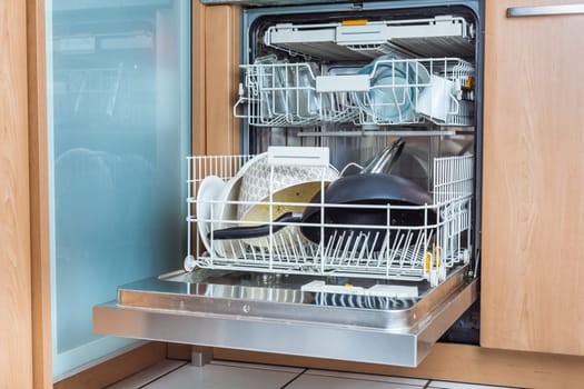 Open modern dishwasher with messy dishes in the kitchen, built-in kitchen dish washing machine