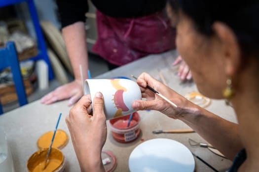 women's hands painting a pottery object