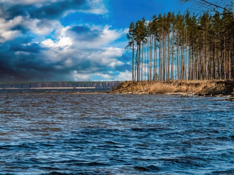 River landscape with forest shore on a cloudy day. Water flow. Dnepr River. Coastal line. Pine tree. Thunderclouds. Sunny day. Weather. Natural landscape. Windy weather.