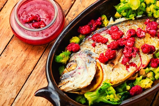 Tasty baked whole fish in fruit marinade on old wooden table