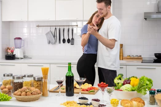 Happy couple in love dancing together in kitchen while preparing and cooking food meal for romantic dinner. Happy family spending time together in weekend