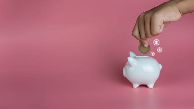A human hand put a coin in a piggy bank on a pink background. Savings and investment concepts.