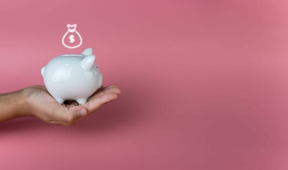 Hand holding a white piggy bank on a pink background. Savings and investment concepts.