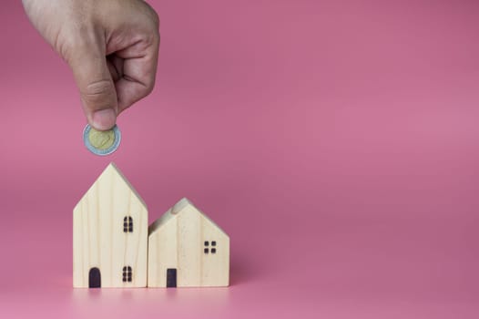 A human hand put a coin in the model house. Ideas for saving money to buy a new home and loans for planning future real estate investments.