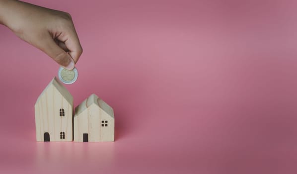 A human hand put a coin in the model house. Ideas for saving money to buy a new home and loans for planning future real estate investments.