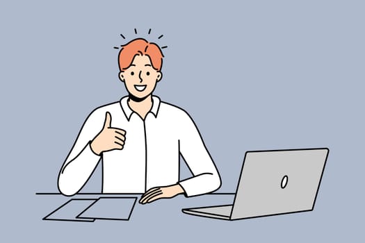 Smiling man at office desk show thumb up