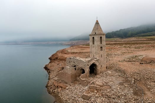 Aerial view of Sau Reservoir, in the Ter River, in the Province of Girona, Catalonia, Spain. After months without rain the level of the swamp is very low. Detail of the church of Sant Roma