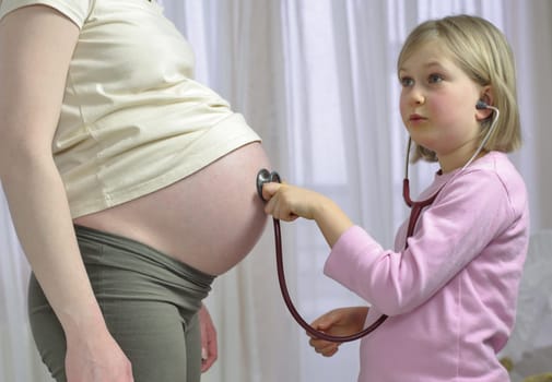 young girl listens to her mums pregnant tummy