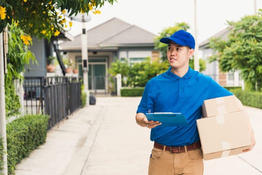 Asian young delivery man courier in uniform hold parcel post boxes service shipment and walking finding and looking for customer home location, Online shopping service concepts