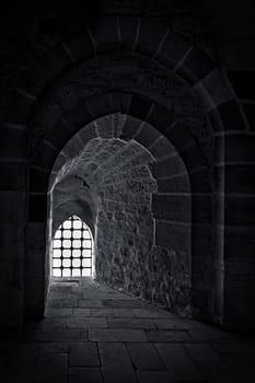 Stone wall with one backlit window with iron grid at one of the passages of an old citadel, Alexandria, Egypt. A fifteenth century defensive fortress located on the Mediterranean sea coast