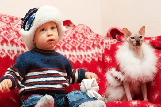 young boy sitting on the red cover with cat dressed like Santa Claus