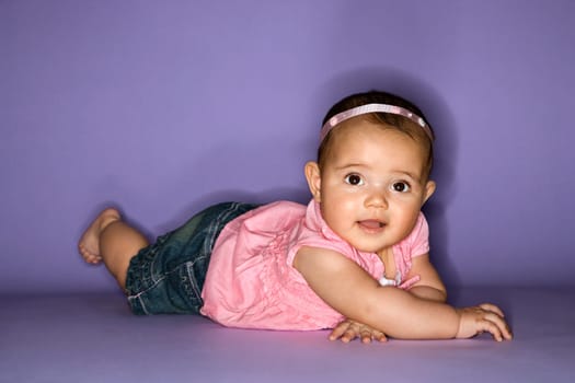 Hispanic female baby lying on stomach.