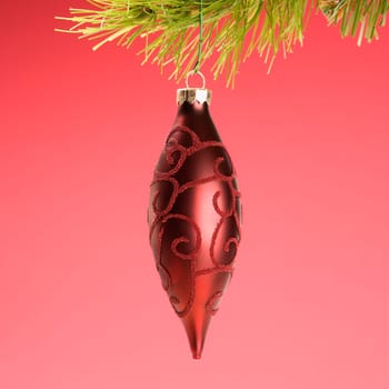 Still life of red Christmas ornament hanging from pine branch.