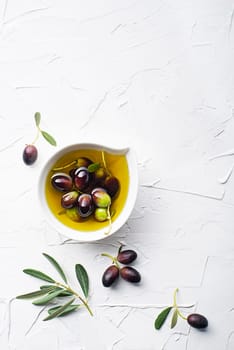 Olive oil in bowl with fresh olives fruit and olive branch on white background