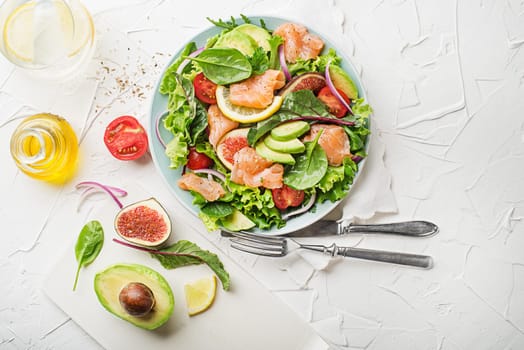 Fresh green salad with smoked salmon, cherry tomatoes, fig and avocado on white table background