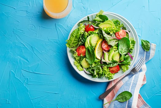 Healthy green salad with avocado and fresh vegetables on blue table close up
