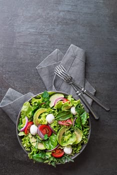 Healthy green salad with avocado, mozzarella cheese and fresh vegetables on dark background
