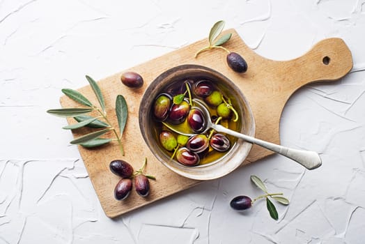 Olive oil in bowl with fresh olives fruit and olive branch on white background close up