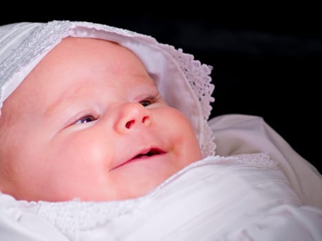 A close up on baby girl in a christening dress on a dark background.