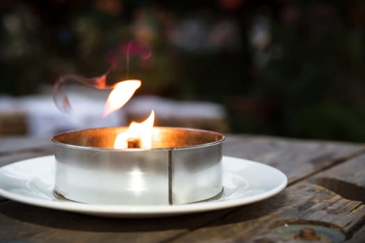 Burning decorative metal candle on blurred background.