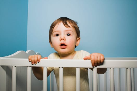 baby standing in his crib over blue wall