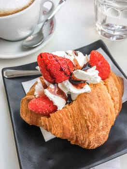 Italian breakfast. Croissant stuffed with whipped cream and strawberries and cappuccino.