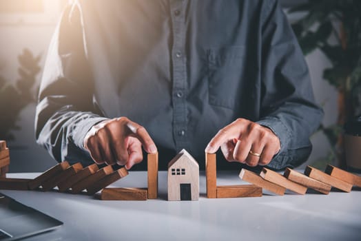 Business risk plan real estate protection. Man hand blocks wood block from many row falling wooden block like domino to house model, Insurance ideas to prevent loss concept