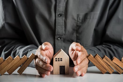 Business risk plan real estate protection. Man hand blocks wood block from many row falling wooden block like domino to house model, Insurance ideas to prevent loss concept