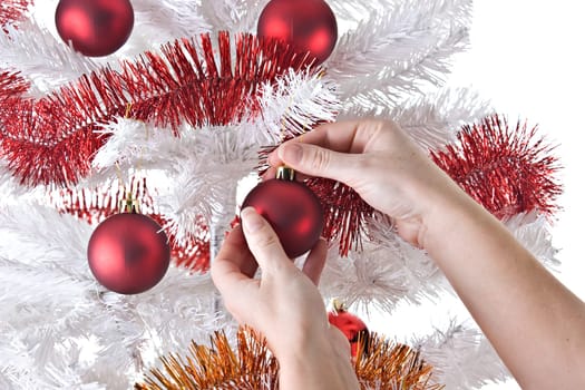 Female hands, hanging ornaments on a white Christmas tree.
