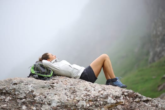 Hiker resting lying on a rock in the foggy mountain