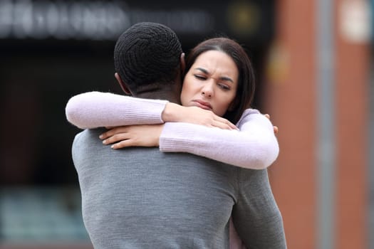 Disappointed woman hugging a black man in the street