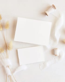 Blank cards near silk ribbons and dried hare's tail grass top view on white, mockup. Boho romantic scene with horizontal cards. Bohemian or close to nature greeting or wedding Invitation