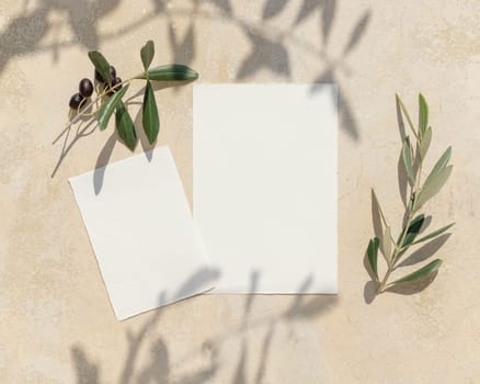 Wedding blank paper cards on a concrete table decorated with olive branches with fruits top view, mockup. Sunny summer mediterranean scene with vertical invitation cards. Flat lay with place for text