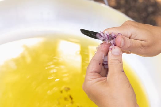 Woman hands chopping red onion over a big frying pan with olive oil close up, copy space. Traditional italian and apulian cousine, cooking for huge family