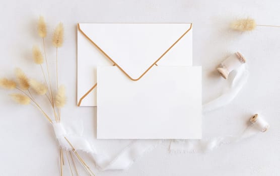 Blank card and envelope near silk ribbons and dried hare's tail grass top view on white, mockup. Boho romantic scene with horizontal cards. Bohemian or close to nature greeting or wedding Invitation